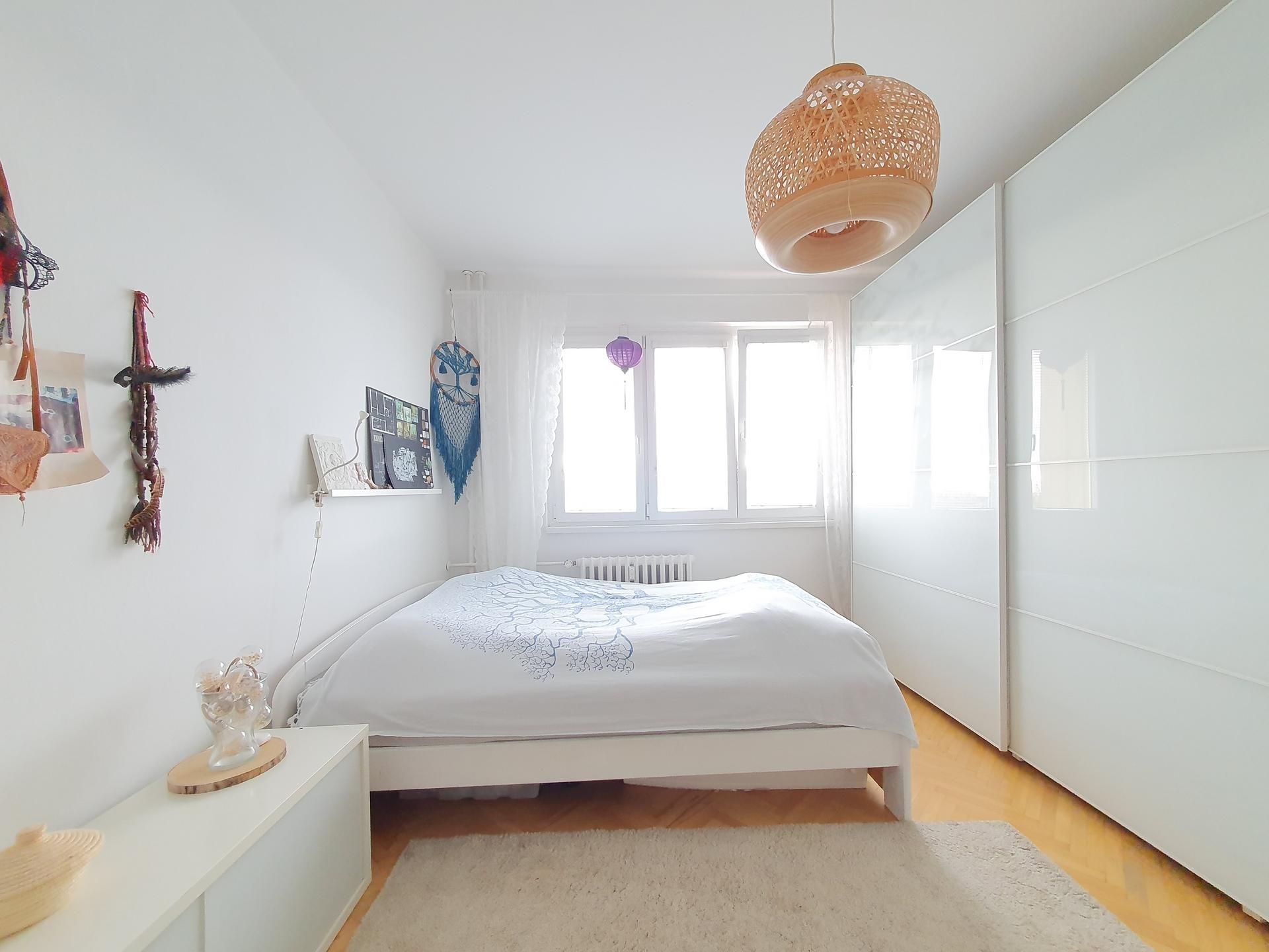 Světlá ložnice s parketovou podlahou, vestavěnými skříněmi a moderním osvětlením, nabízí útulný a stylový prostor k bydlení.