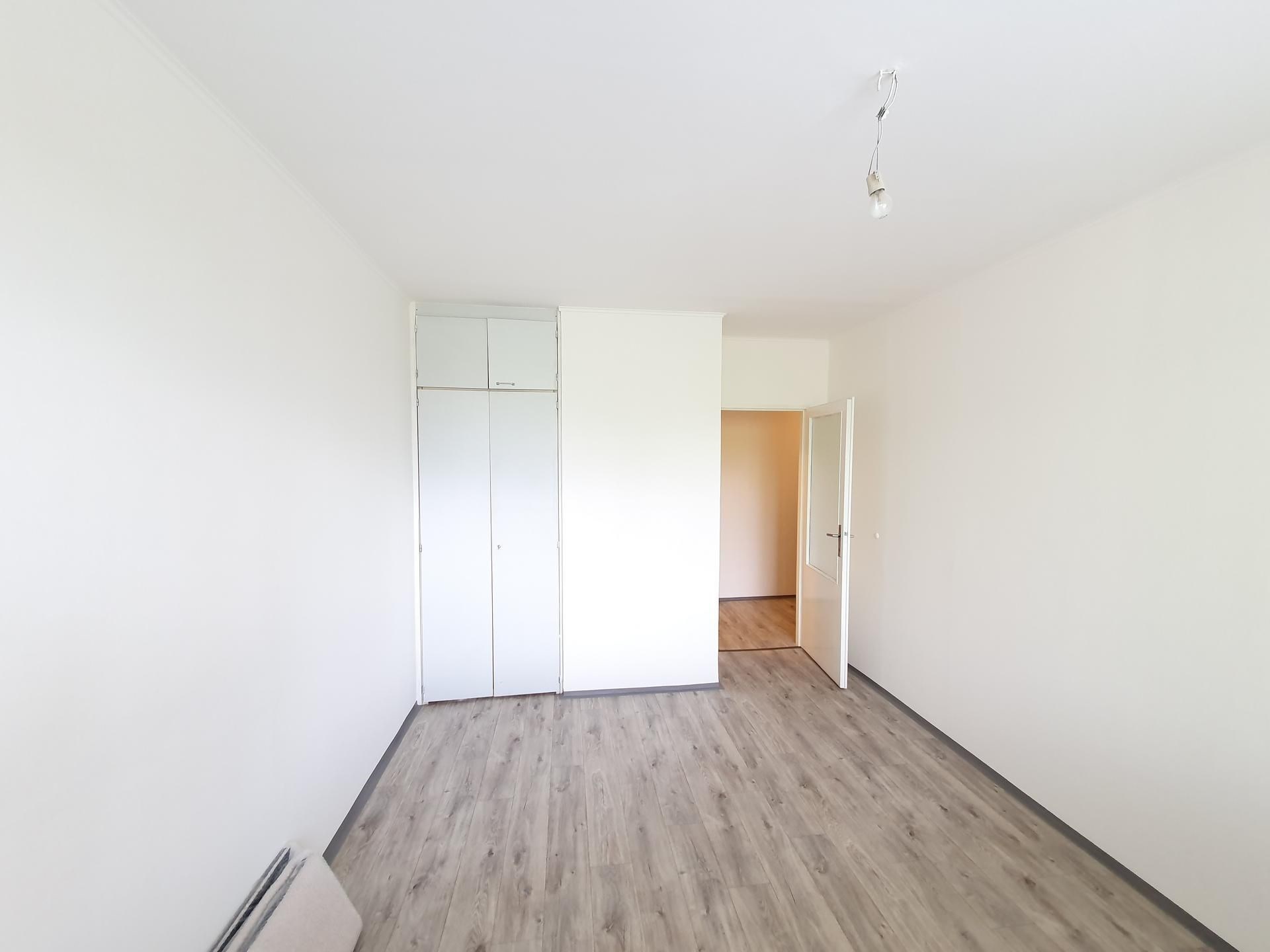 Prázdný pokoj s parketovou podlahou, světlé stěny, vestavěné skříně a otevřené dveře, moderní interiér.
