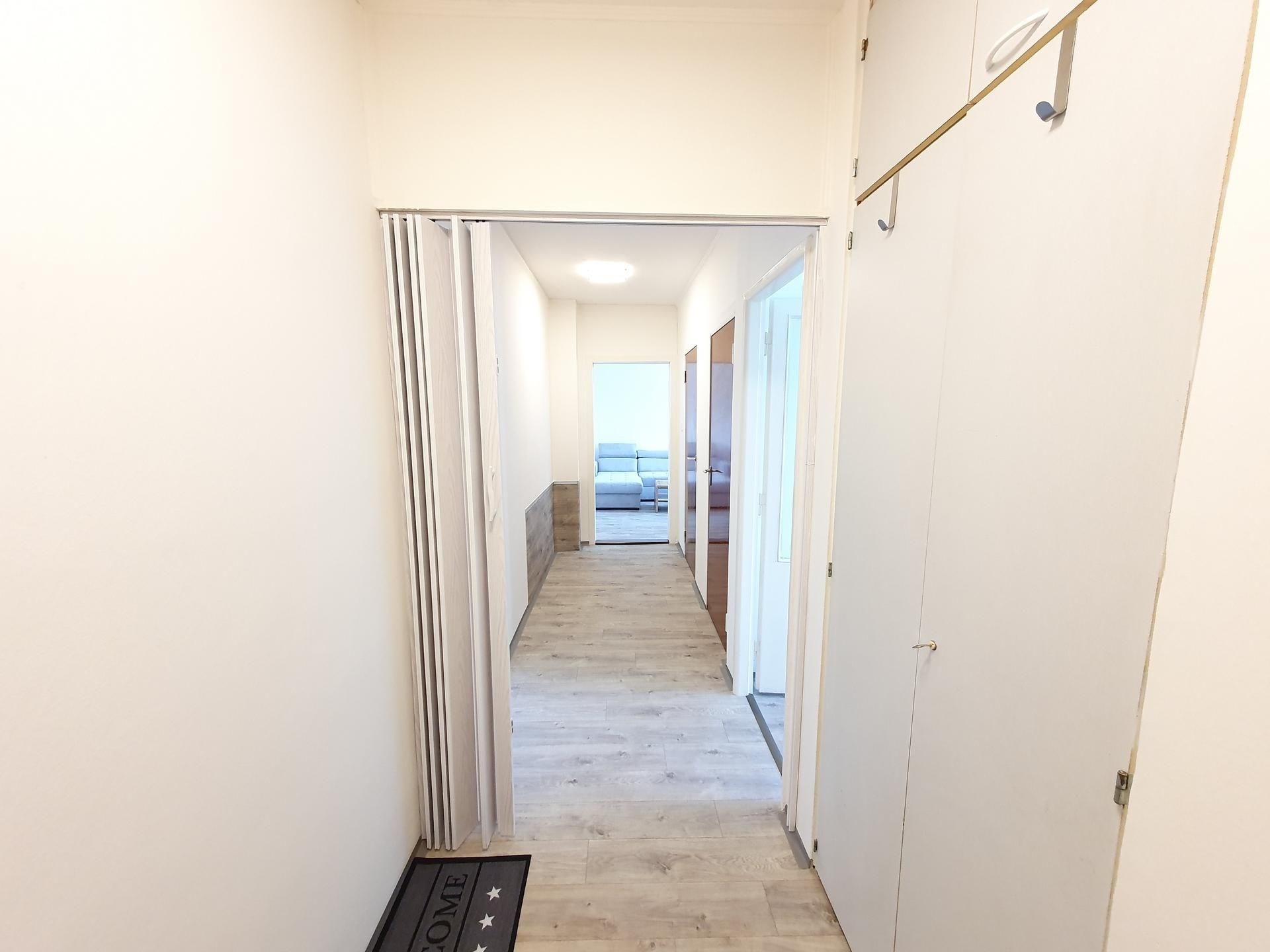 Úzká chodba s vestavěnými skříněmi, dřevěnou podlahou a světlými stěnami, vedoucí do obývacího pokoje, moderní design
